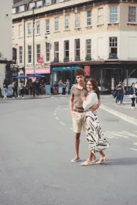 Two people embrace in the middle of a city street during their complimentary engagement photo shoot, with pedestrians and city buildings in the background.