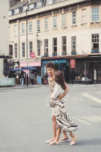 Two individuals embracing on a city street with shops in the background during their complimentary engagement photo shoot.