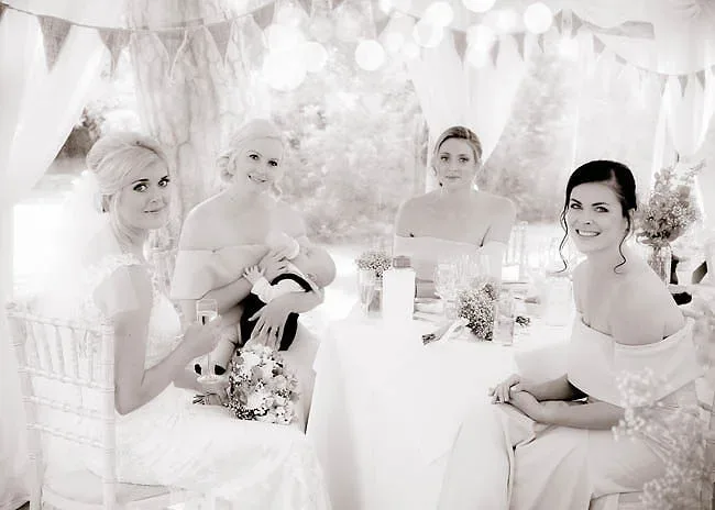 A black and white photo of bridesmaids sitting at a table, captured by Orchardleigh, the talented wedding photographer.