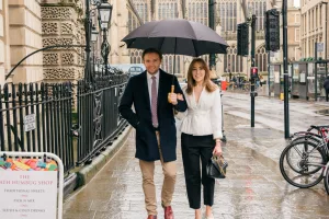 A man and woman strolling down the street with an umbrella, captured by a Guildhall Bath Wedding Photographer.