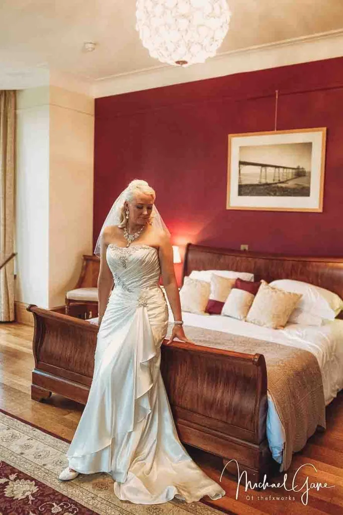 A bride posing in front of a bed in a room with red walls at Coombe Lodge Weddings