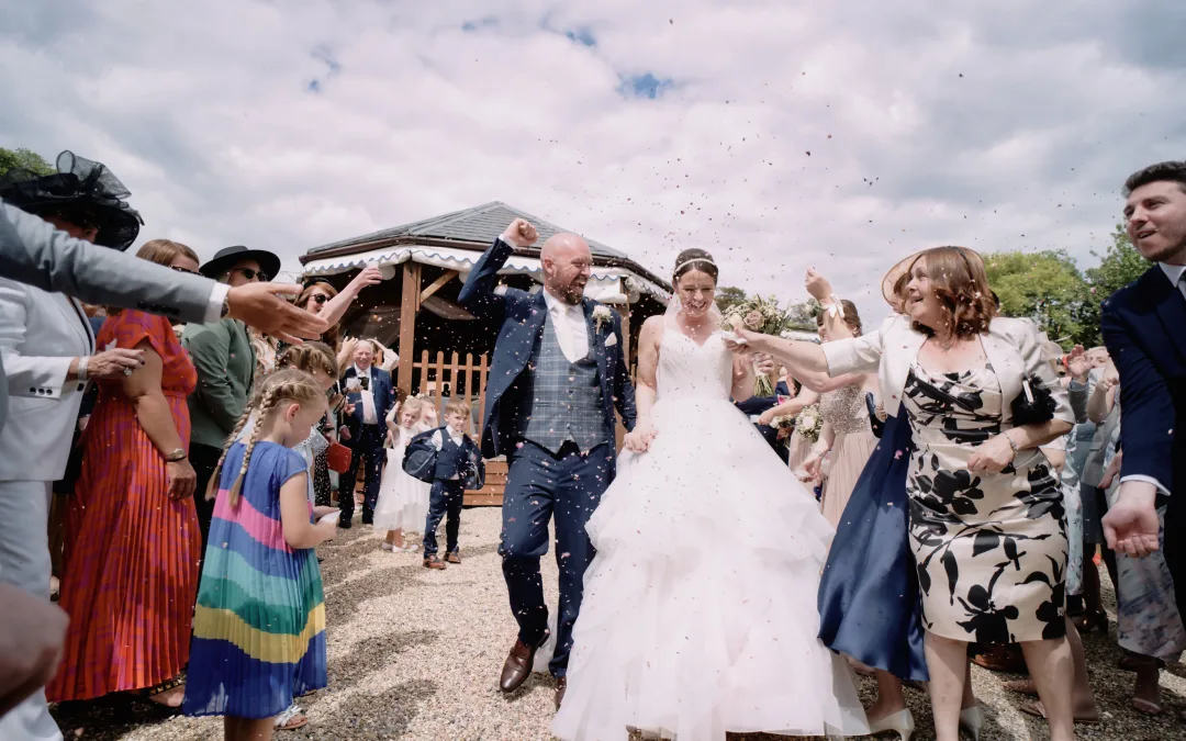 A bride and groom leave the Orchardleigh House ceremony with confetti thrown at them, captured by a talented wedding photographer.