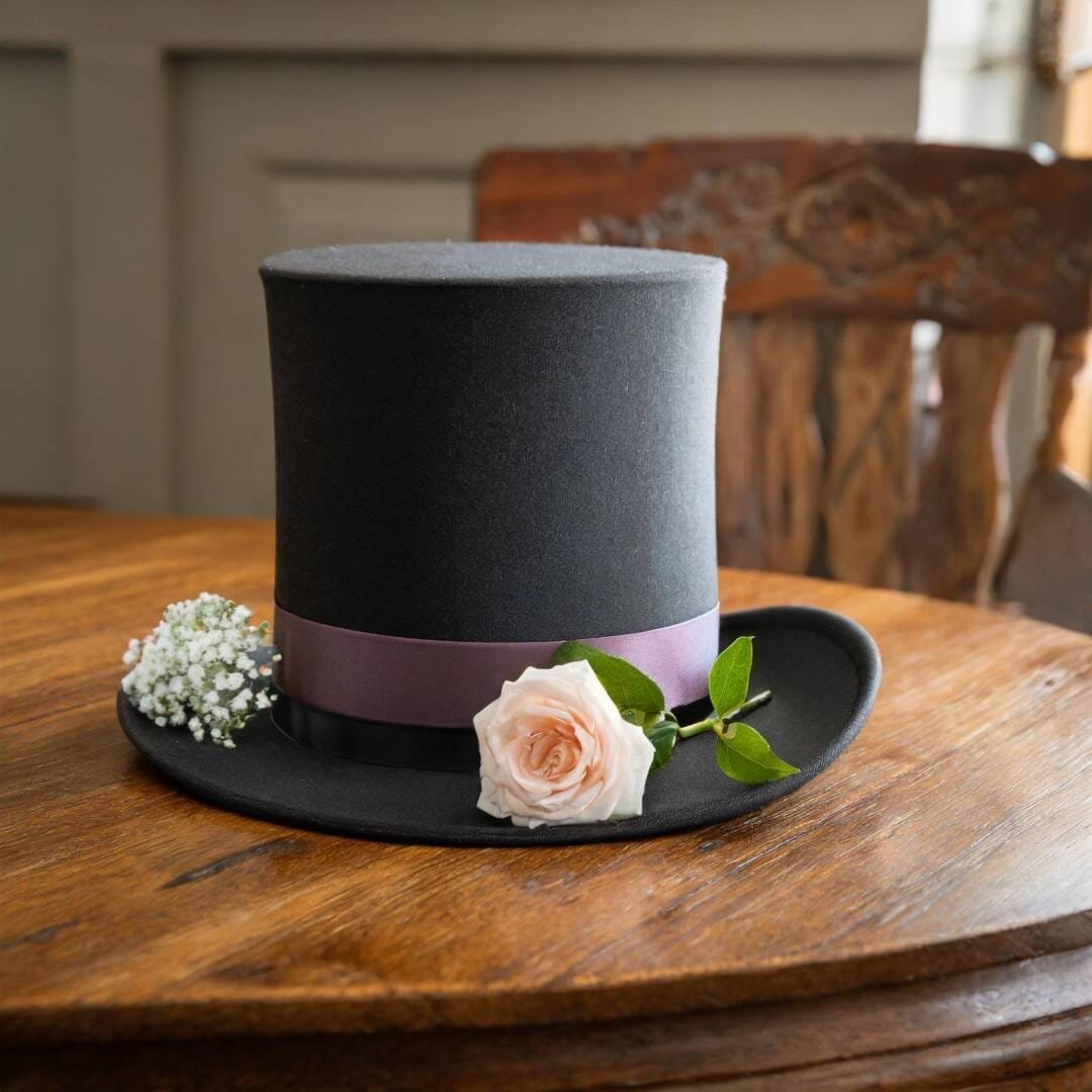 A black top hat with a pink band and a light pink rose rests on a wooden table, capturing the essence of creative photography in every detail, making it perfect for your next photography block project.