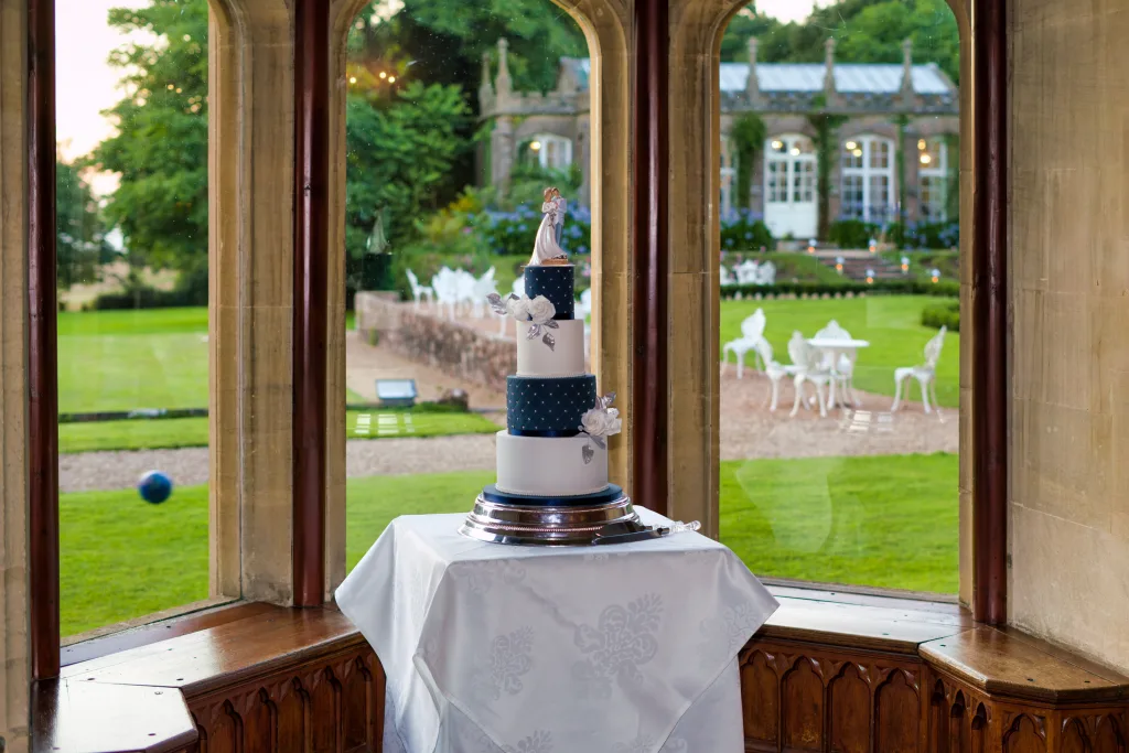 A discounted wedding cake sitting on a table in front of a window at St. Andrie's park.