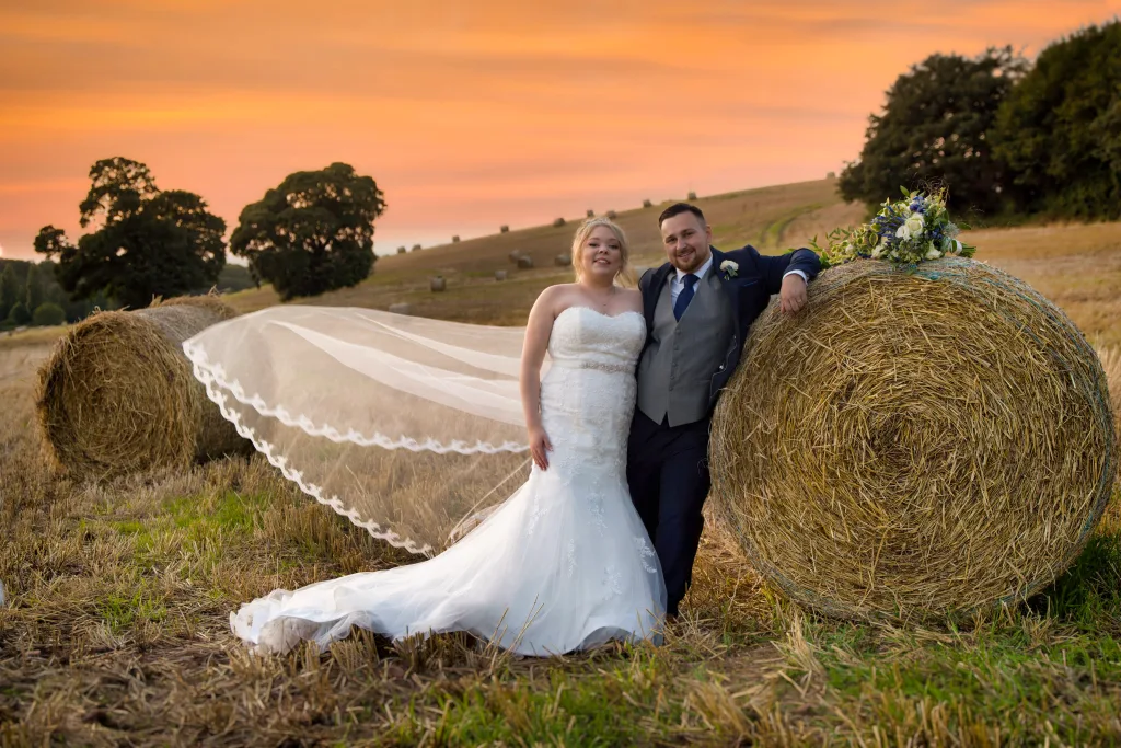 A bride and groom pose in front St. Andrie's park with hay bales at sunset during their wedding photography session.