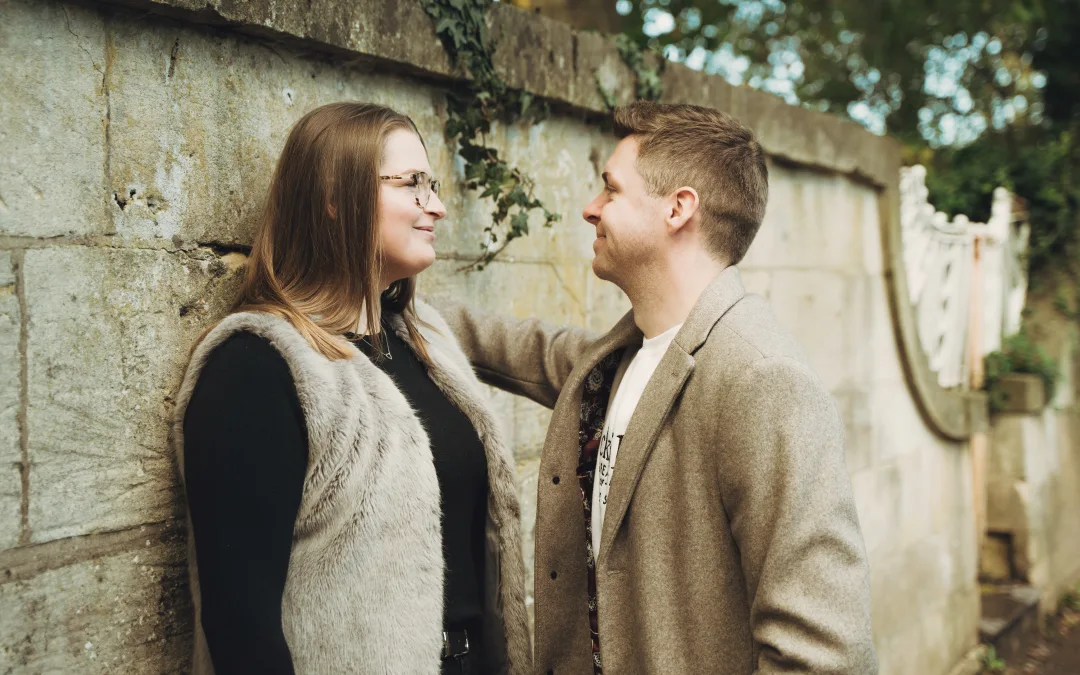 An engaged couple standing next to a stone wall. Wedding Engagement Photo shoot in Bath