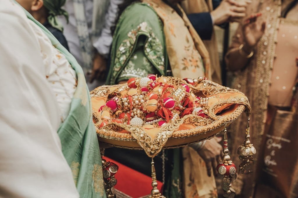 A person in traditional attire holds a decorated tray filled with colorful trinkets and ornaments, surrounded by other people in similarly festive clothing, all captured beautifully using Fuji Cameras for weddings.