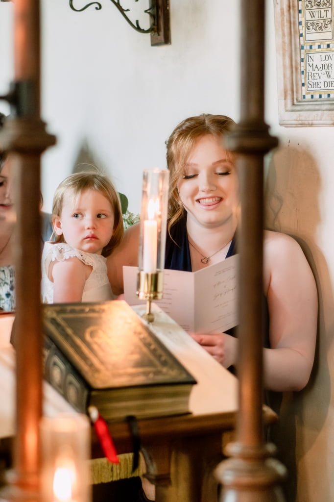 A woman reads from a book beside a lit candle, with a young girl looking on, in a warmly lit room with vintage decor at Orchardleigh.
