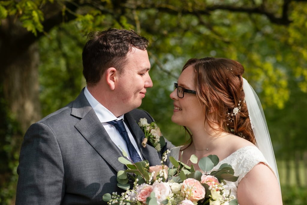 A bride and groom gazing at each other affectionately, holding a bouquet, outdoors on a sunny day, captured by their wedding photographer at Orchardleigh.