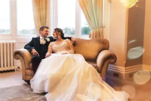 A bride and groom captured by Wedding Photographer Orchardleigh, sitting on a couch in a large room.