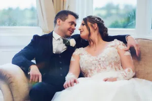 A wedding photographer capturing a beautiful moment of a bride and groom sitting on a couch in front of a window at Orchardleigh.