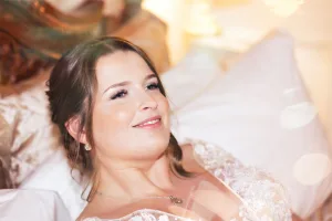 A radiant bride, captured by the talented Wedding Photographer at Orchardleigh Estate, lays on a luxurious bed with a joyous smile beaming across her face.