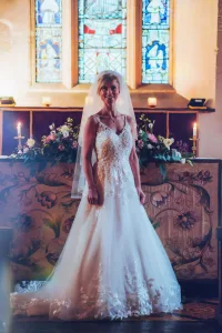 A bride in a wedding dress standing in front of a stained glass window at Orchardleigh House.