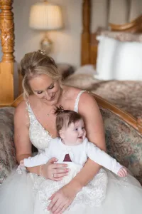 A woman in a wedding dress holding a baby on a bed, captured beautifully by the Wedding Photographer at Orchardleigh.
