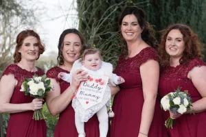 Wedding Photographer capturing bridesmaids in burgundy dresses holding a baby at Orchardleigh.