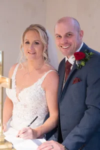 A bride and groom signing their wedding vows in front of a cross captured by the Wedding Photographer at Orchardleigh.