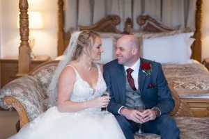 A bride and groom posing on a bed in a hotel room captured by the Wedding Photographer at Orchardleigh.