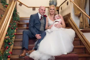 Wedding photographer capturing a bride, groom, and their baby on the stairs at Orchardleigh estate.