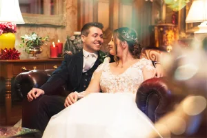 A bride and groom, captured by a talented wedding photographer at Orchardleigh estate, share an intimate moment while sitting on a cozy living room couch.