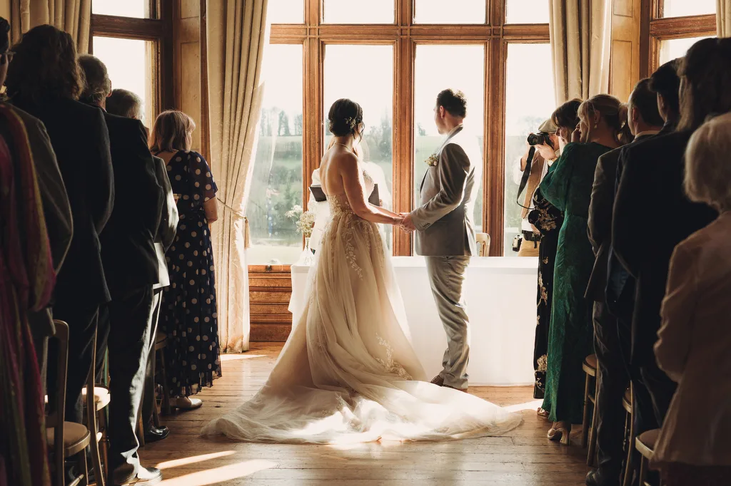 Orchardleigh345 Bride and groom holding hands, receiving guests' attention in a sunlit room at Orchardleigh House.