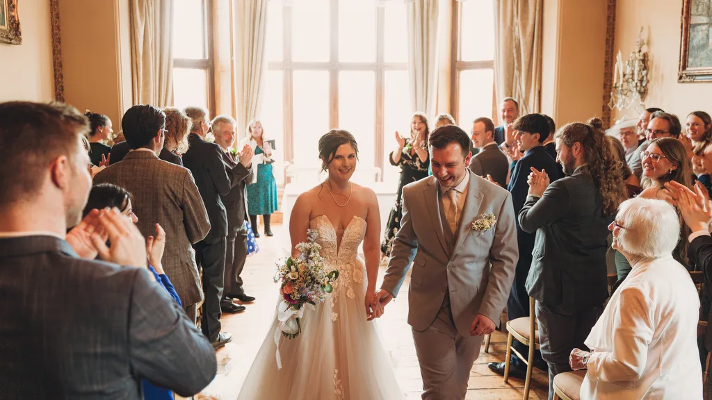 Orchardleigh399 A newlywed couple walking down the aisle at Orchardleigh House, surrounded by applauding guests.