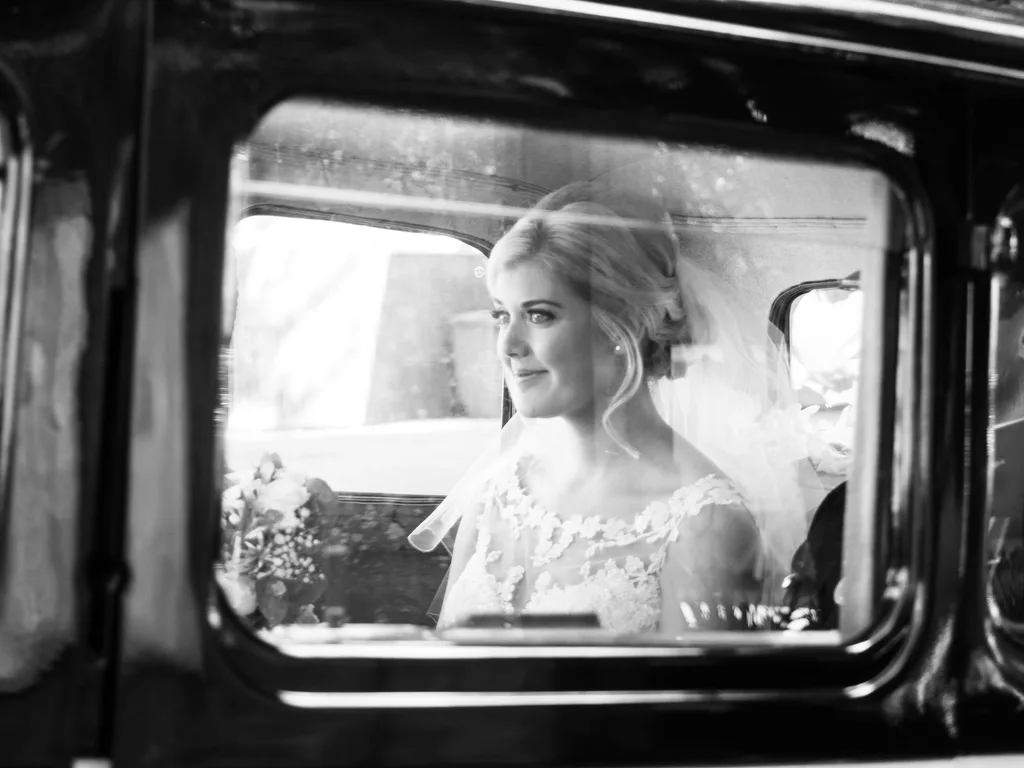 A world-class wedding photographer captures a bride looking out of the window of a vintage car, freezing this beautiful moment in time.