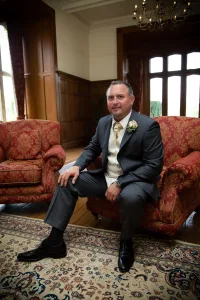 A man in a suit sitting on a red chair at St. Andrie's park wedding Photography discount