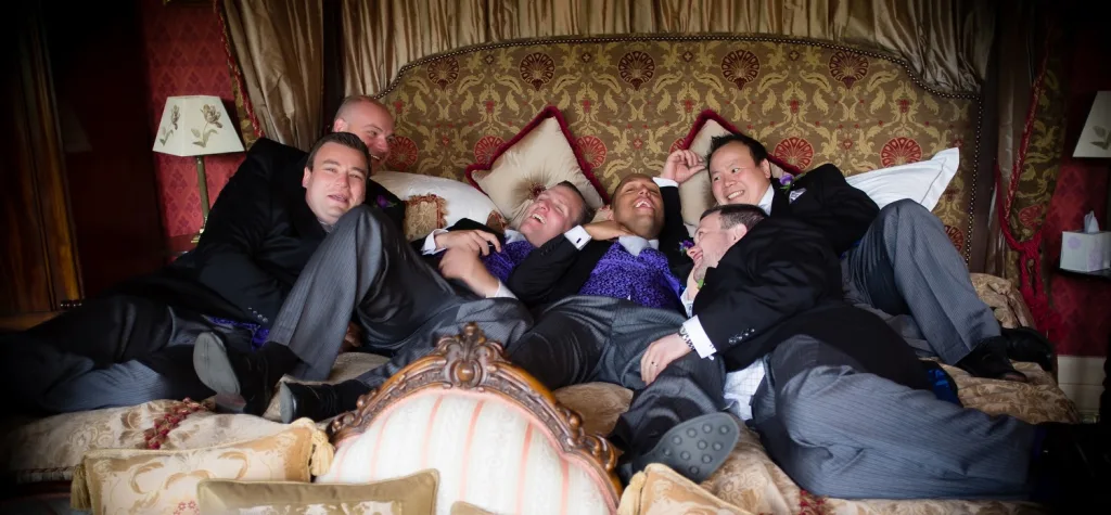 A group of groomsmen laying on a bed in St. Andrie's Park and Babington House