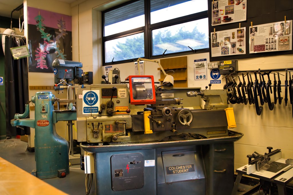 A student in a classroom is engaged in a discussion while seated at a desk with open books and notebooks. Other students are seen in the background, capturing an authentic moment perfect for school marketing photography.