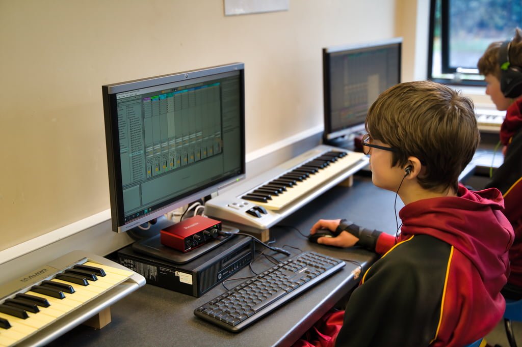 A student in a classroom is engaged in a discussion while seated at a desk with open books and notebooks. Other students are seen in the background, capturing an authentic moment perfect for school marketing photography.