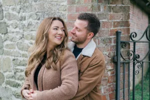 An engaged couple embracing in front of a stone wall captured by a talented Stourhead wedding photographer.