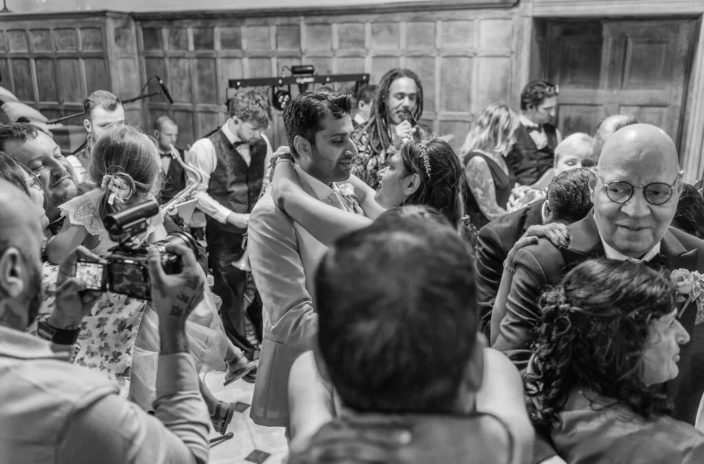 A black-and-white photo of a crowded dance floor at a wedding reception, captured by Farleigh House Wedding Photographer, shows various pairs of people dancing closely while others snap pictures to capture the joyous moments.