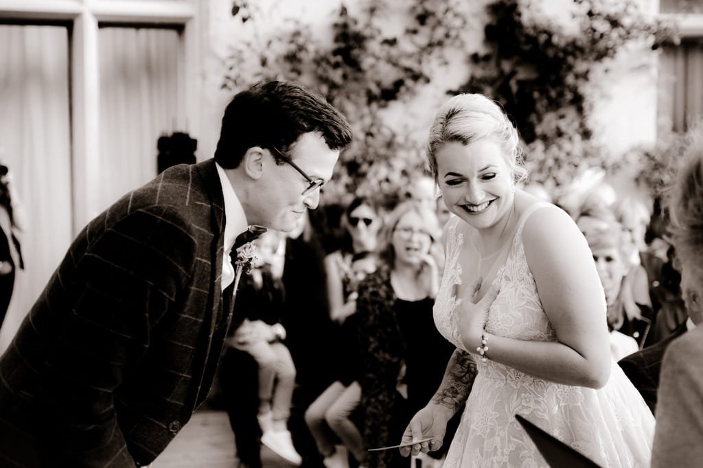 Black and white photo of a smiling couple bending down towards a seated person, surrounded by a small group of onlookers in an outdoor setting at Orchardleigh House Weddings.