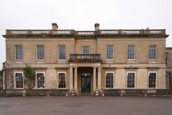 A large, historic building perfect for Hartham Park Weddings, with two stories and a symmetrical facade. The entrance is adorned with pillars, and there are multiple windows on each floor. The elegant exterior is beige with weathered stone details.