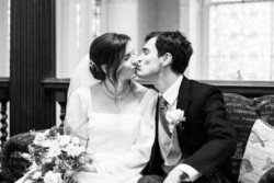At Hartham Park Weddings, the bride and groom share a tender kiss while seated, the bride elegantly holding her bouquet.