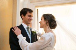 Evoto A bride and groom smile at each other indoors, with sunlight streaming through a window behind them, capturing the timeless charm of Hartham Park Weddings.