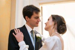 Evoto A bride and groom share a tender moment indoors at Hartham Park Weddings, gazing into each other's eyes. The bride is wearing a veil and a white dress, while the groom is dressed in a dark suit with a boutonniere.
