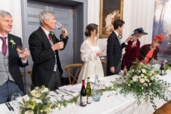 At a Hartham Park Weddings reception, people stand around a beautifully decorated table, toasting with wine glasses in an elegant and formal setting.