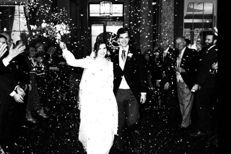 At Hartham Park Weddings, a bride and groom smile radiantly as they walk through a crowd showering them with confetti.