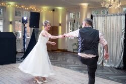 An older couple dances together in a well-lit event hall at Elmhay Park Weddings, with the woman in a white dress and the man in a vest and dress shirt.
