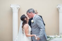 A bride and groom kiss in front of two white columns during their Bath Spa Hotel Weddings ceremony, with the officiant standing behind them.