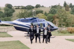 A group of groomsmen standing in front of a helicopter at Orchardleigh House wedding.