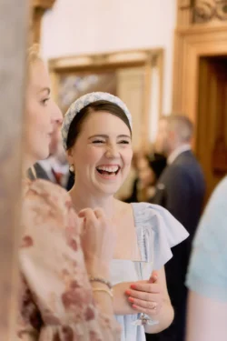 At a party, a woman is laughing with another woman, captured beautifully by an Orchardleigh House Wedding Photographer.