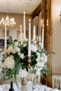 A gorgeous centerpiece adorned with white flowers and candles graces a table at an Orchardleigh House wedding, captured beautifully by a talented photographer.