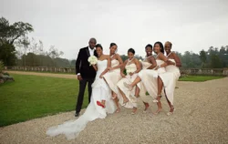 www.thefxworks.co.uk A bride and groom pose with bridesmaids, all lifting their legs to show red-soled heels, in an outdoor setting at Orchardleigh House Weddings.