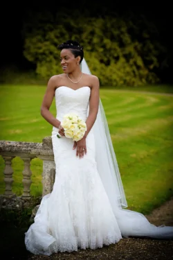www.thefxworks.co.uk A bride in a white strapless gown with a long veil holding a bouquet of flowers, smiling outdoors at Orchardleigh House Weddings.