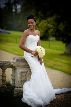 www.thefxworks.co.uk A bride in a strapless white gown smiling while holding a bouquet, standing next to a stone balustrade outdoors at Orchardleigh House.