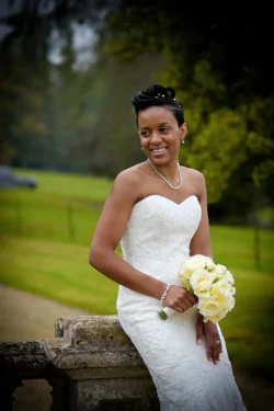 www.thefxworks.co.uk A bride in a strapless wedding dress holding a bouquet of white roses while smiling outdoors at Orchardleigh House Weddings.