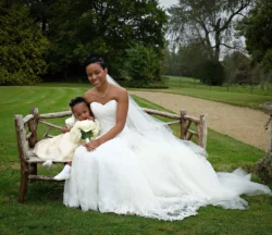 www.thefxworks.co.uk A bride in a white gown sitting on a wooden bench at Orchardleigh House Weddings with a young child in a formal dress holding a bouquet.