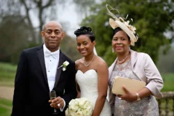 www.thefxworks.co.uk Three individuals at an Orchardleigh House wedding ceremony, with the bride in a white gown flanked by an older man in a tuxedo and an older woman in a dress with a hat, all